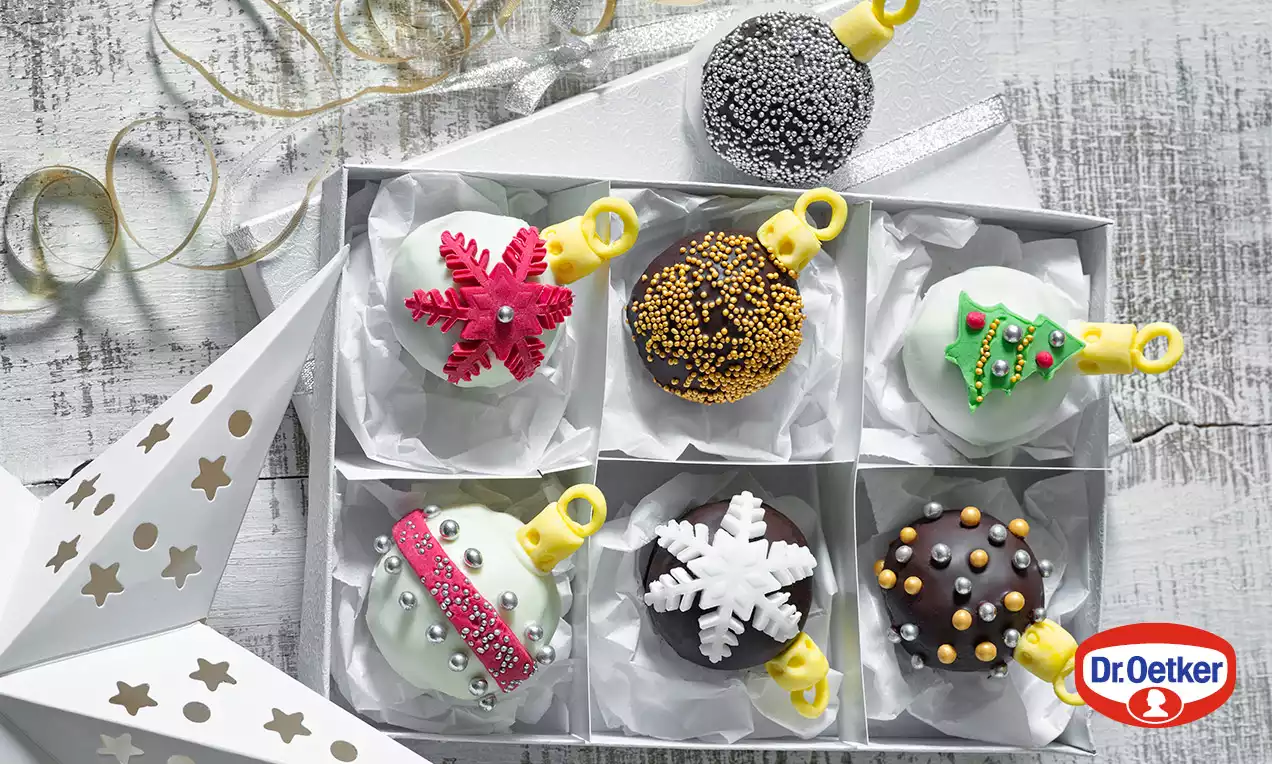 Vianočné guľôčky s farebnou polevou a zdobením v tvare vločiek, hviezdičiek a stromčekov, uložené v bielej darčekovej krabici so zlatými detailmi