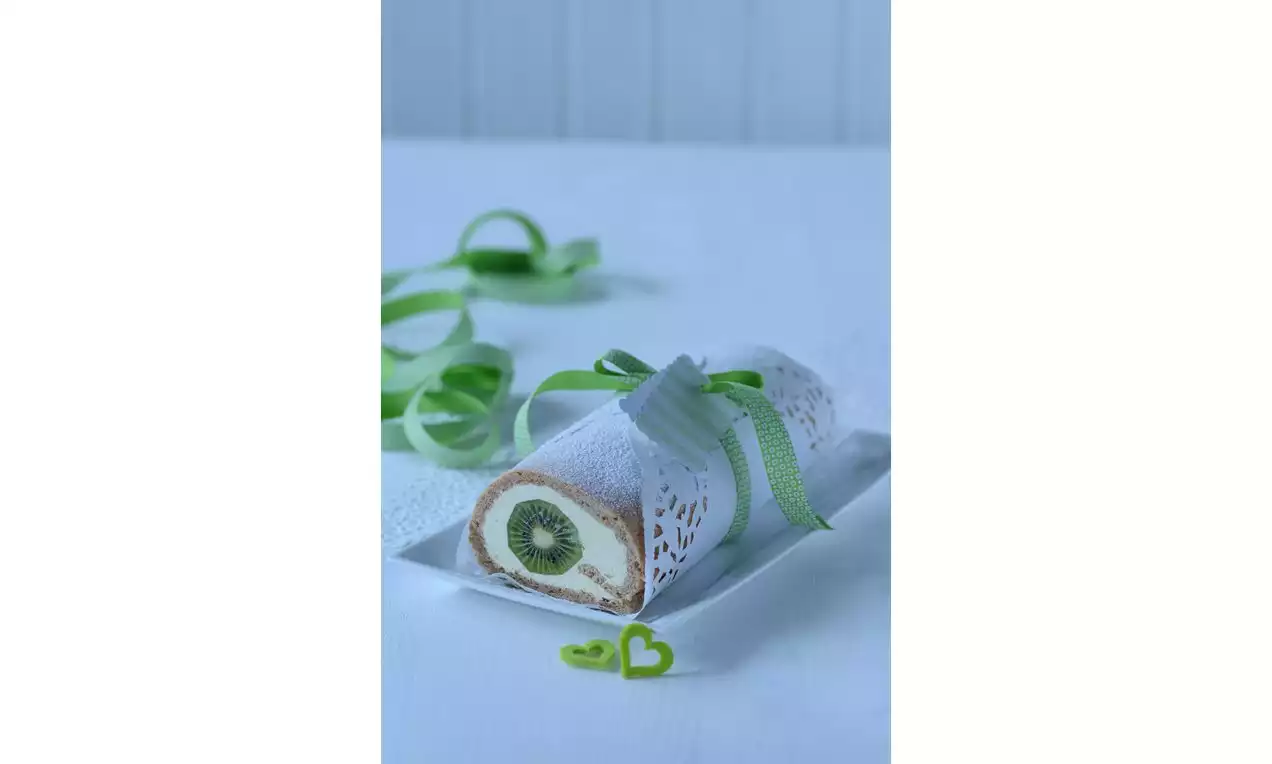 Roláda s bílým krajkovým ozdobným obalem, světlým piškotovým těstem, plněná krémem a zeleným plátkem kiwi, ozdobená zelenou stuhou