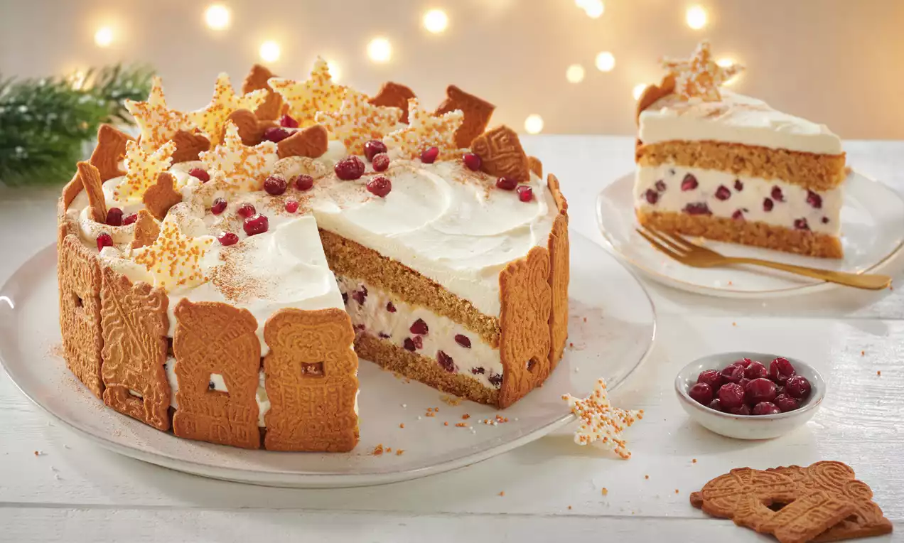 Käse-Sahne-Torte mit goldbraunem Spekulatiusrand, weißer Cremehaube, roten Beeren und dekorativen Sternen auf einem weißen Teller