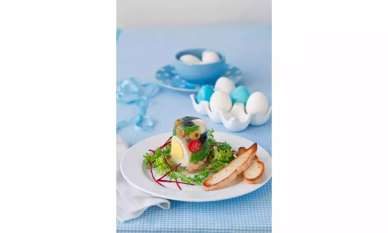 Priehľadná želatína so zeleninou, vajíčkom a petržlenom na tanieri s čerstvým šalátom, kúskami hrianky a modro-bielym pozadím