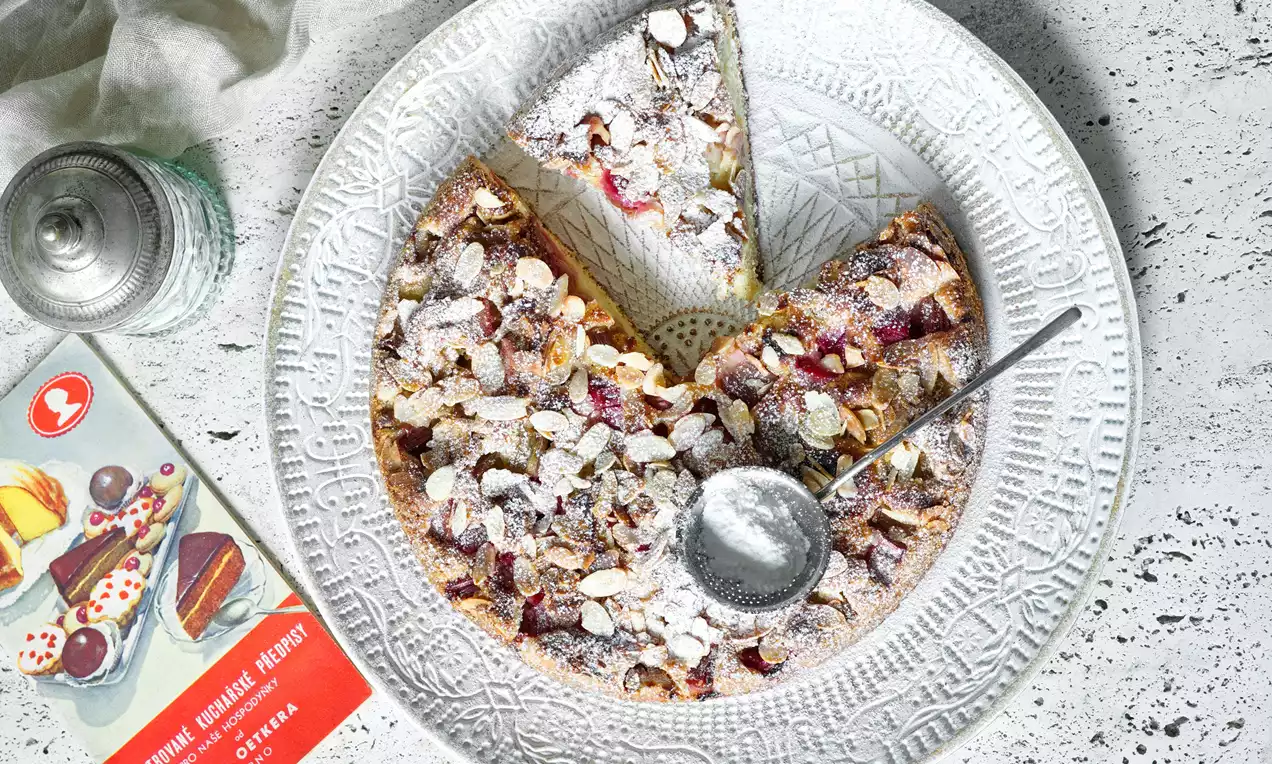 Rebarborový koláč s posýpkou z pražených mandlí a práškového cukru na bielo vzorovanom tanieri s lyžičkou vloženou do stredu