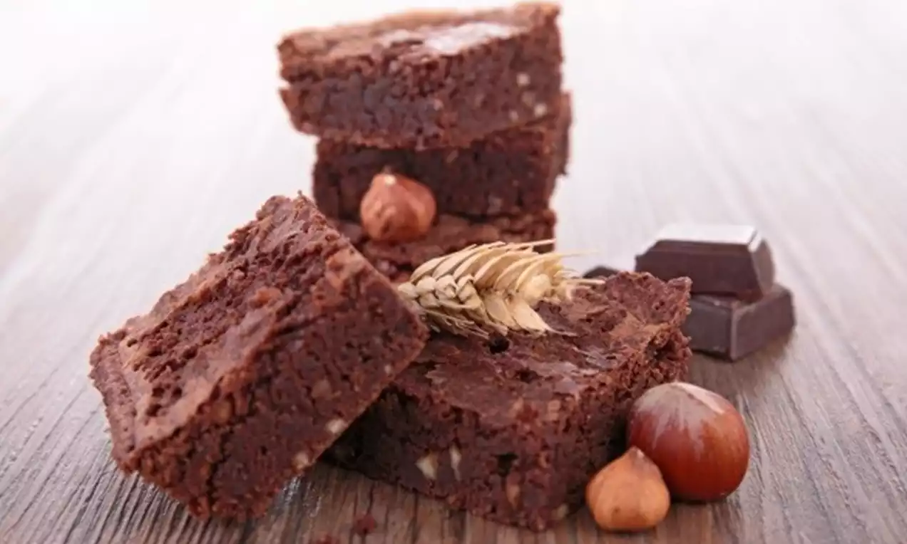 Rich, dark chocolate hazelnut brownies with a dense, fudgy texture, stacked on a wooden surface, surrounded by hazelnuts and chocolate pieces