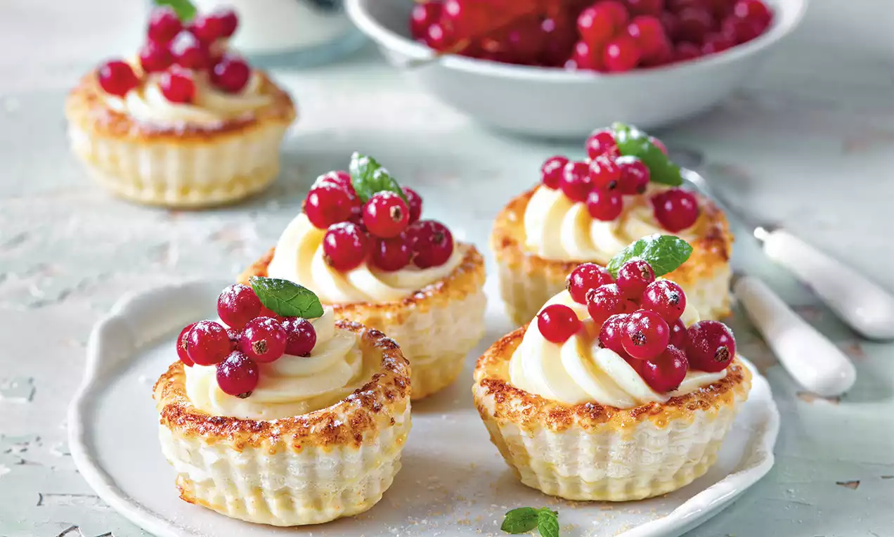 Krehké košíčky zlatohnedej farby s krémovou náplňou, ozdobené červeným ríbezľom a lístkami mäty na bielom tanieri