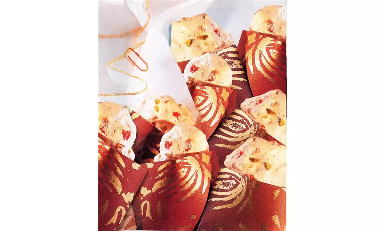 Altın ve kırmızı motifli sargılara yerleştirilmiş, hafif pütürlü dokulu, badem parçacıklarıyla bezenmiş krem rengi bezeler