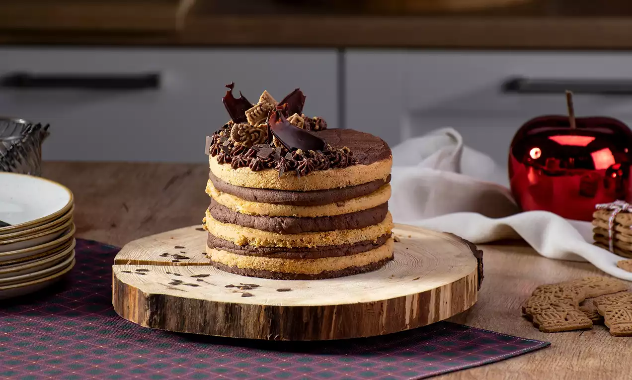 Spekulatius-Schoko-Torte mit abwechselnden braunen Schokoschichten und goldgelben Spekulatiusböden, garniert mit Schokospänen auf Holzplatte