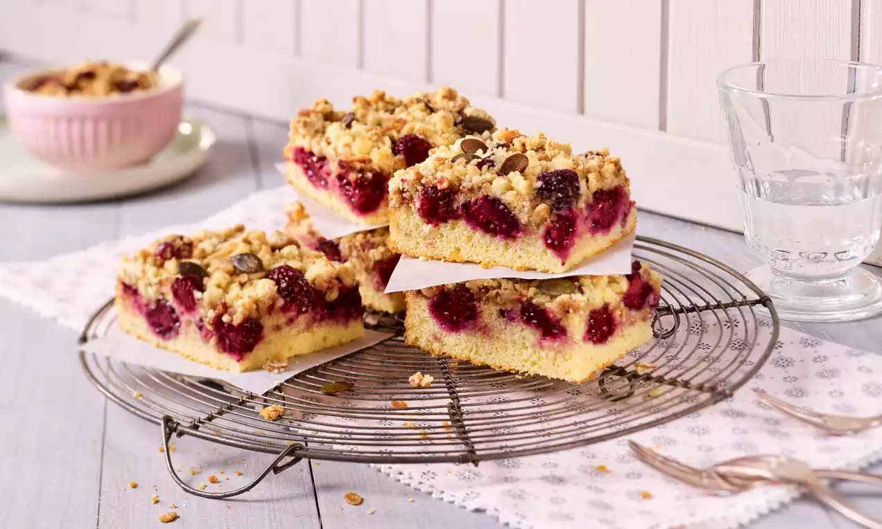 Vier rechteckige Brombeer-Müsli-Schnitten mit goldbraunen Streuseln und saftigen lila Brombeeren auf einem Kuchengitter angerichtet