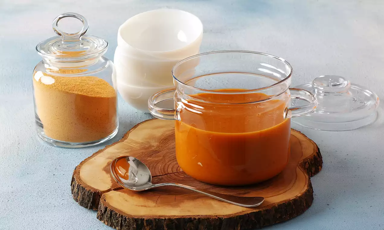 Cam kapta yoğun bir kıvamda tarhana çorbası, yanında tarhana tozu dolu cam kavanoz, bir kaşık ve kesilmiş ahşap sunum tabağı üzerinde