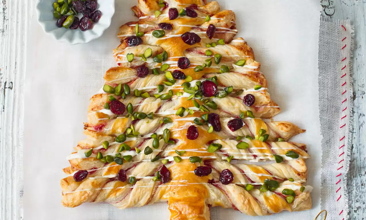 Zlatistý vánočný stromček z lístkového cesta s pretkanými prúžkami, zdobený sušenými brusnicami, zelenými pistáciami a bielou polevou