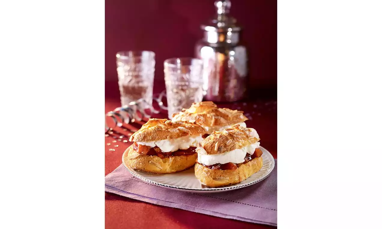 Zlatnosmeđi ekleri nepravilnog oblika s hrskavom korom, ispunjeni bijelom kremom i tamnim nadjevom na pjegavom bijelom tanjuru