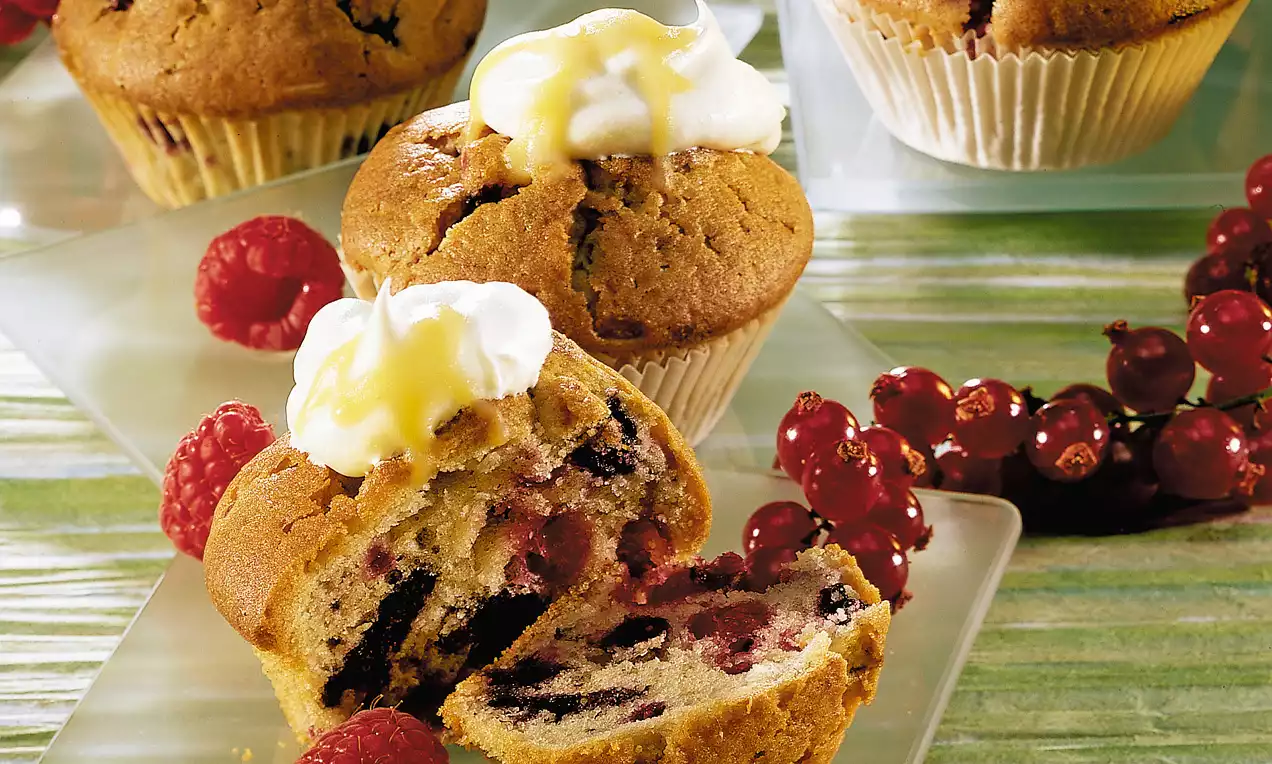 Tortini dorati con frutti di bosco e cuore morbido, guarniti con crema bianca e decorati con lamponi e ribes su piatti verde chiaro