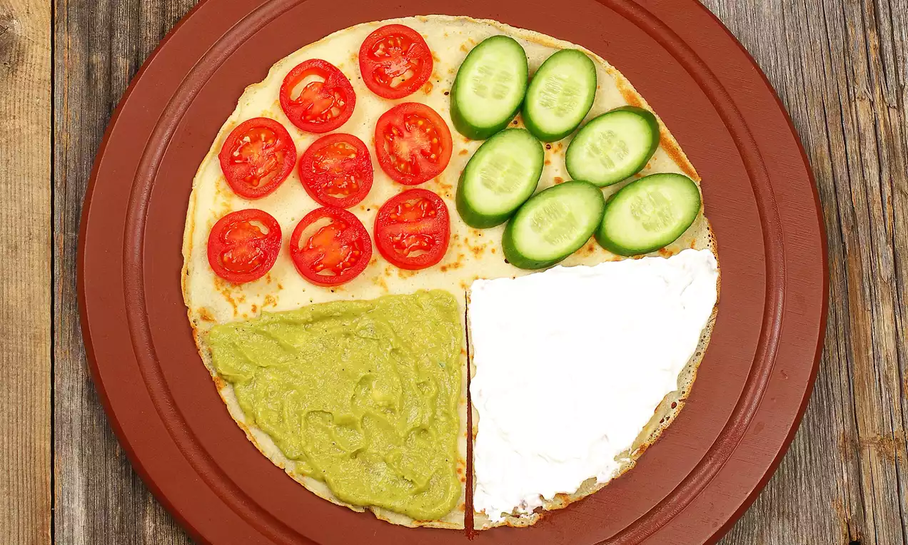 Dört eşit bölgeye ayrılmış bir krep; domates, salatalık dilimleri, avokado püresi ve krem peynirle süslenmiş kırmızı bir tabakta