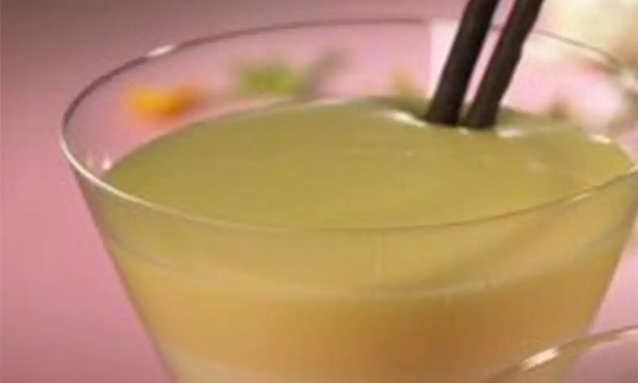 Crème lisse et brillante jaune pâle dans un verre transparent, décorée de fins bâtonnets chocolatés et d'une légère touche florale