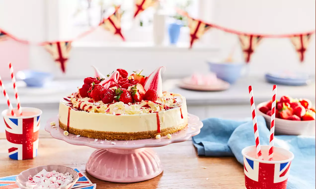 Eton Mess cheesecake with smooth cream filling on a biscuit base, topped with meringue shards, fresh raspberries and drizzled sauce