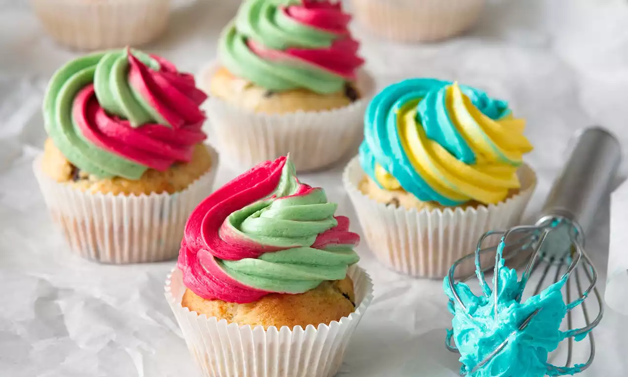Cupcake v papierovom košíčku, s krémom v špirálovitých vrstvách zeleného, červeného, žltého a modrého odtieňa, položený na bielom papieri