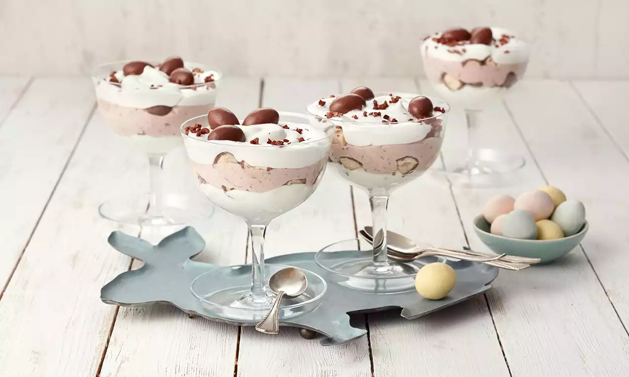 Schichtdessert in Glas mit weißer und hellbrauner Creme, gefüllt mit Schoko Bon®-Stücken, garniert mit Schokolade auf metallischem Tablett