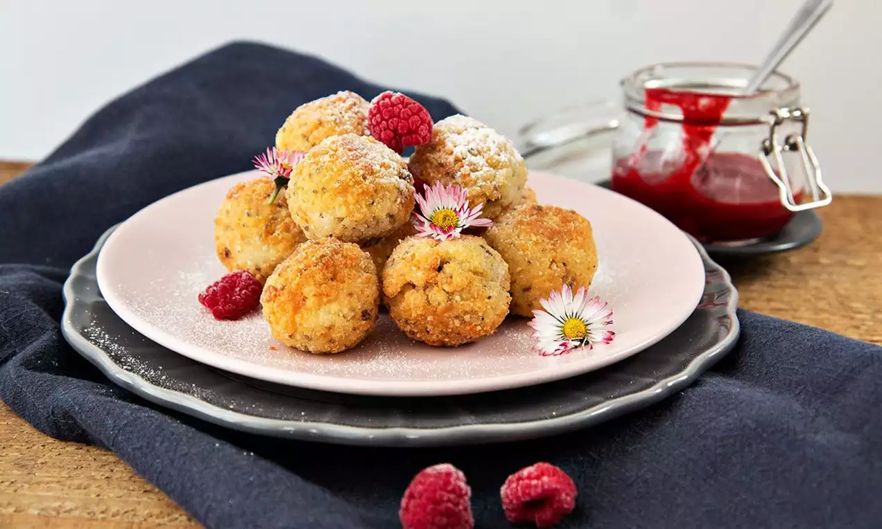 Guľaté arancini zlatisté s chrumkavou textúrou, usporiadané na ružovom tanieri, ozdobené malinami, kvietkami a práškovým cukrom bez prílohy