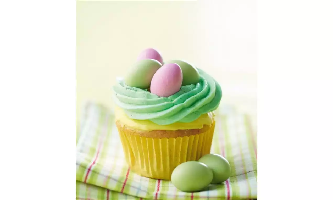 Gul cupcake med grønn glasur toppet med rosa og grønne eggformede sjokolader på rutete pastellfarget serviett