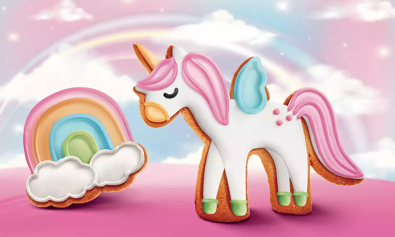 Pastelový perník jednorožca s ružovou hrivou, modrým krídlom a dúhou, detailne zdobený cukrovou polevou na ružovom pozadí