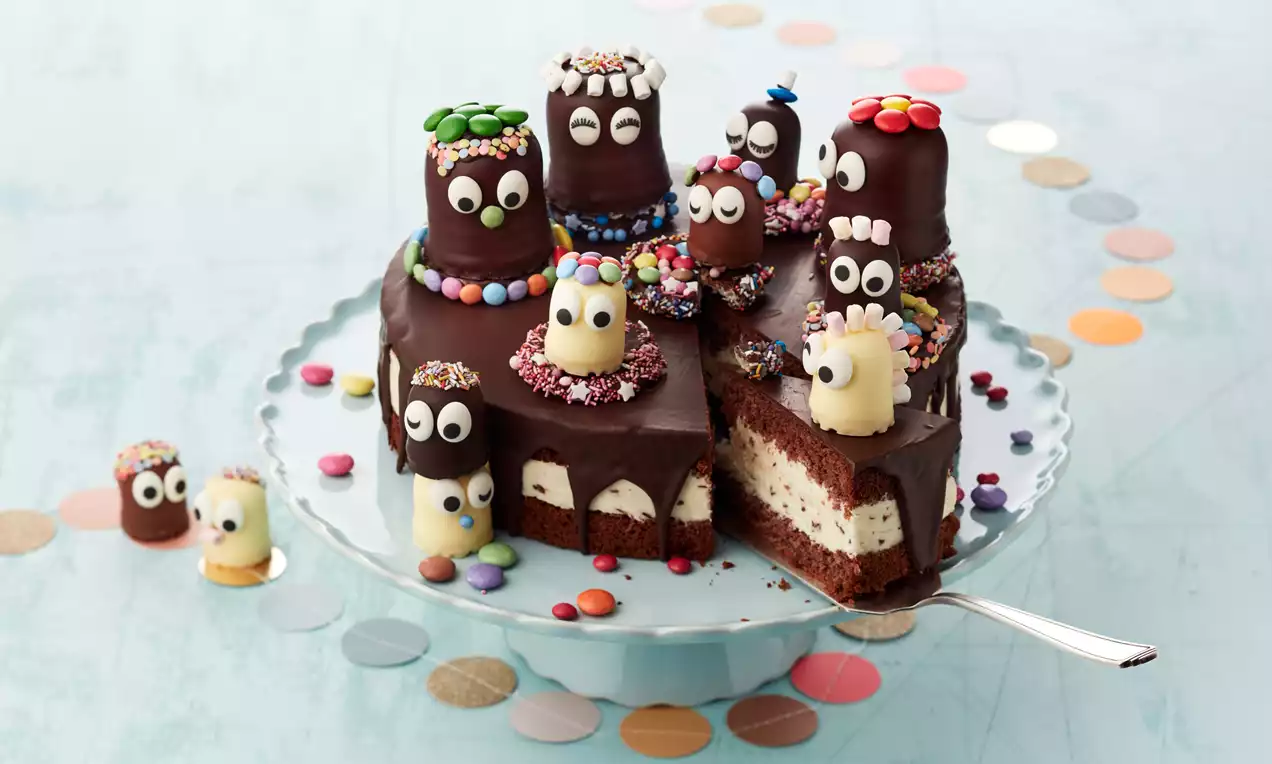 Schokokusstorte mit saftigem Schokobiskuit, heller Sahnefüllung, Schokoglasur, Schokoküssen und bunten Streuseln auf weißem Teller