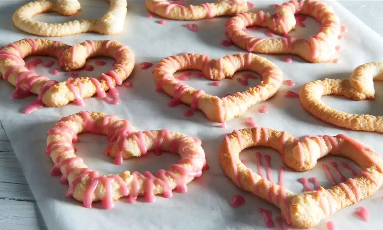 Marcipánové srdiečka svetlohnedej farby, miestami jemne zlatisté, s ružovou polevou rozliatou v prúžkoch na papieri na pečenie