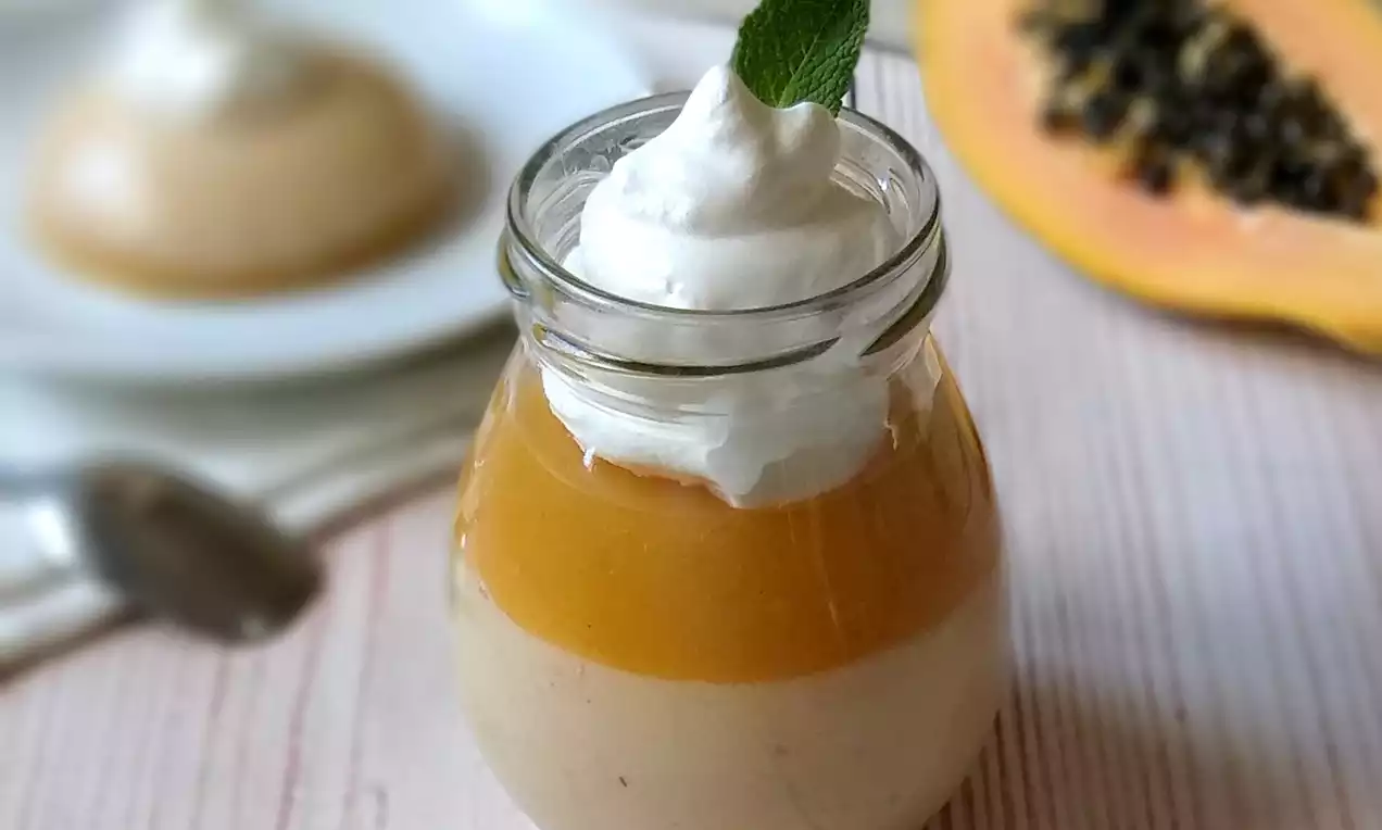 Papájový dezert v sklenenom pohári s vrstvou krémového základu, lesklou oranžovou papájovou polevou, šľahačkou a lístkom mäty