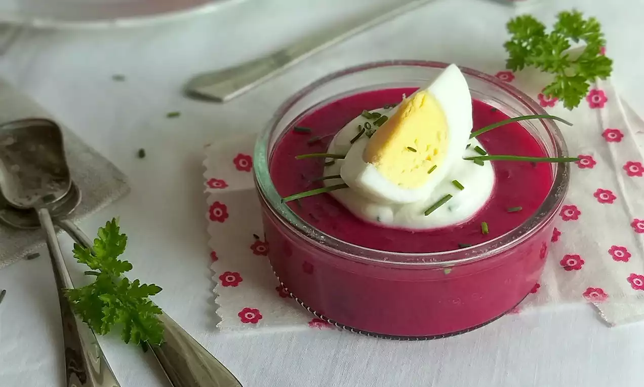 Řepný aspik sýto ružovej farby v sklenenej miske, ozdobený plátkom vajíčka, kopčekom smotany, pažítkou a čerstvou petržlenovou vňaťou