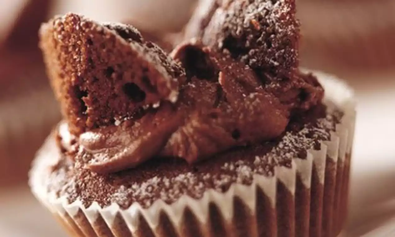 Cupcake chocolaté moelleux dans une caissette, crème au cacao en volutes, décoré de deux morceaux de gâteau saupoudrés de sucre