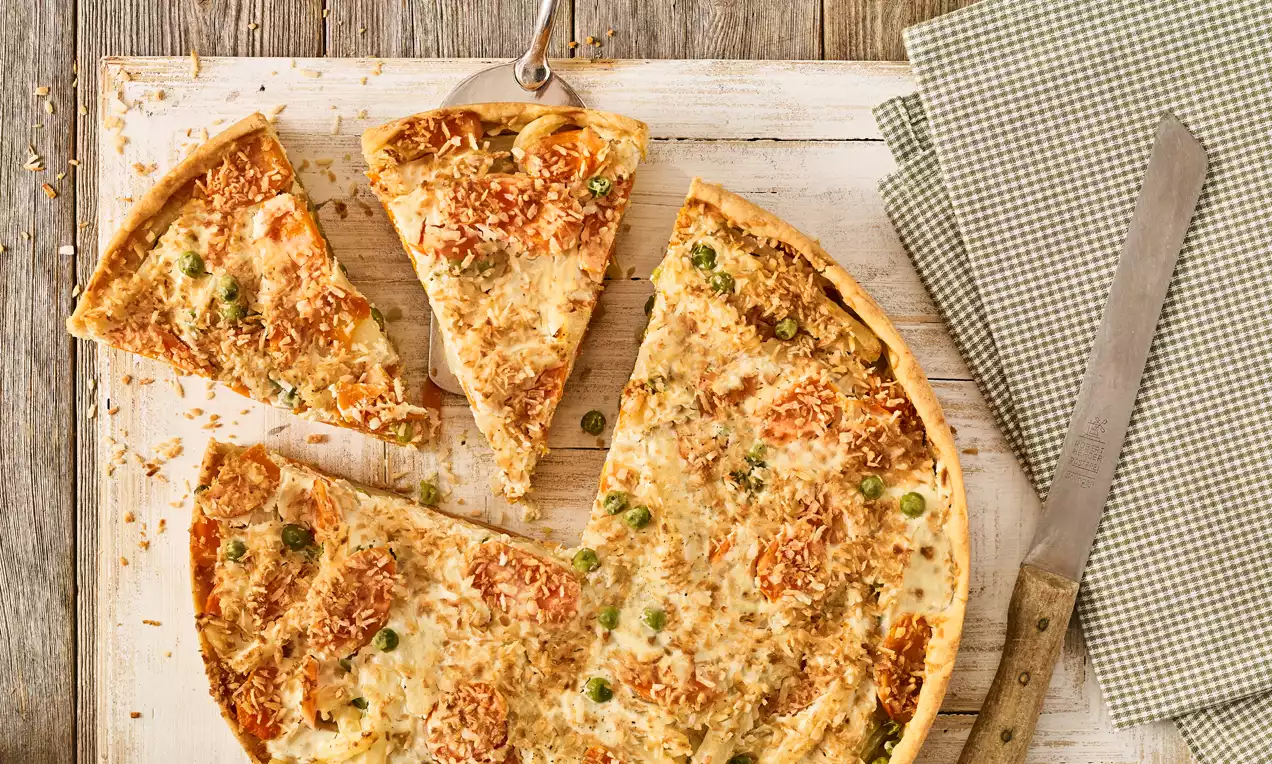 Veganska quiche svijetlosmeđe kore, posuta zapečenim komadićima povrća i hrskavim mrvicama na drvenoj podlozi uz zelenu tkaninu