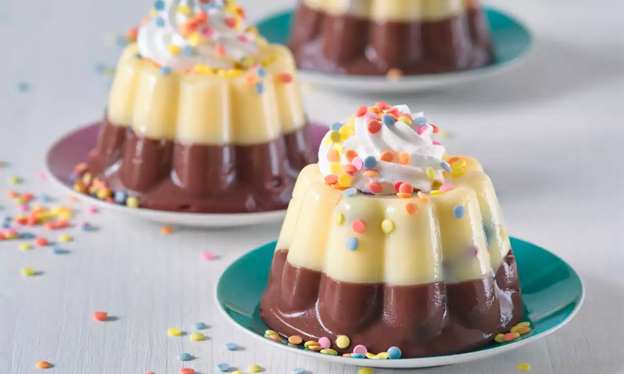 Dvoubarevný dezert s tmavou čokoládovou a světlou vanilkovou vrstvou, zdobený šlehačkou a barevnou cukrovou posypkou na barevném talíři
