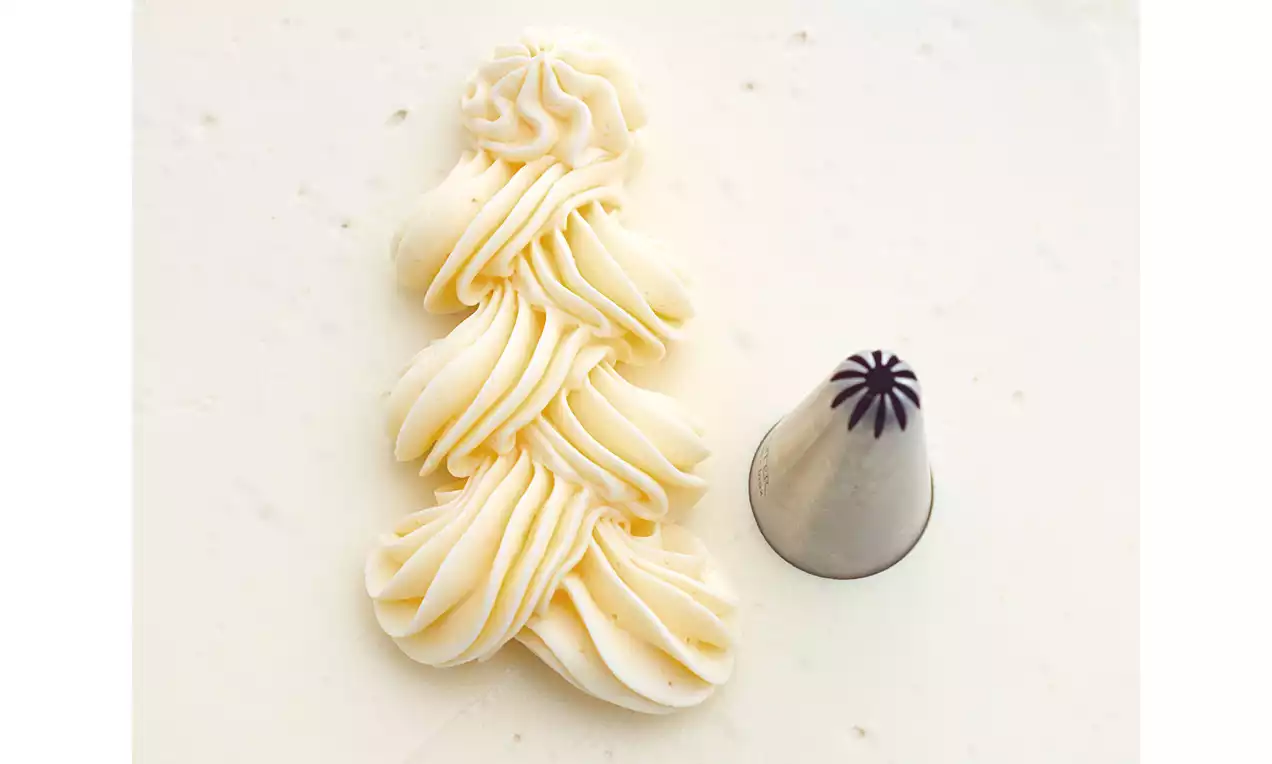 Vanillefarbene Sahne mit gerillter, sternförmiger Struktur, sauber auf hellem Untergrund gespritzt neben einer Metall-Sterntülle