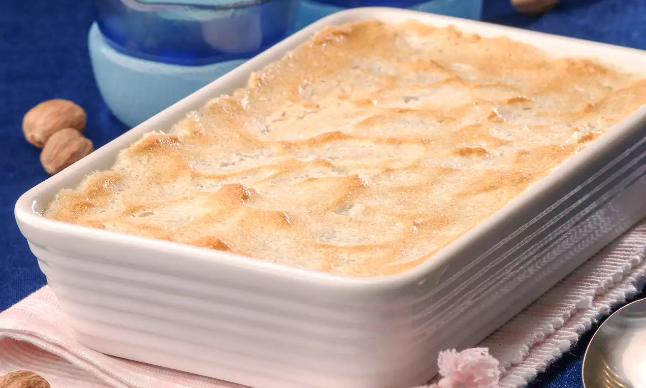 Fırınlanmış üstü hafif altın rengi kabarık mereng kaplı, dikdörtgen beyaz seramik kapta sunulan tatlı, pembe örtü üzerinde