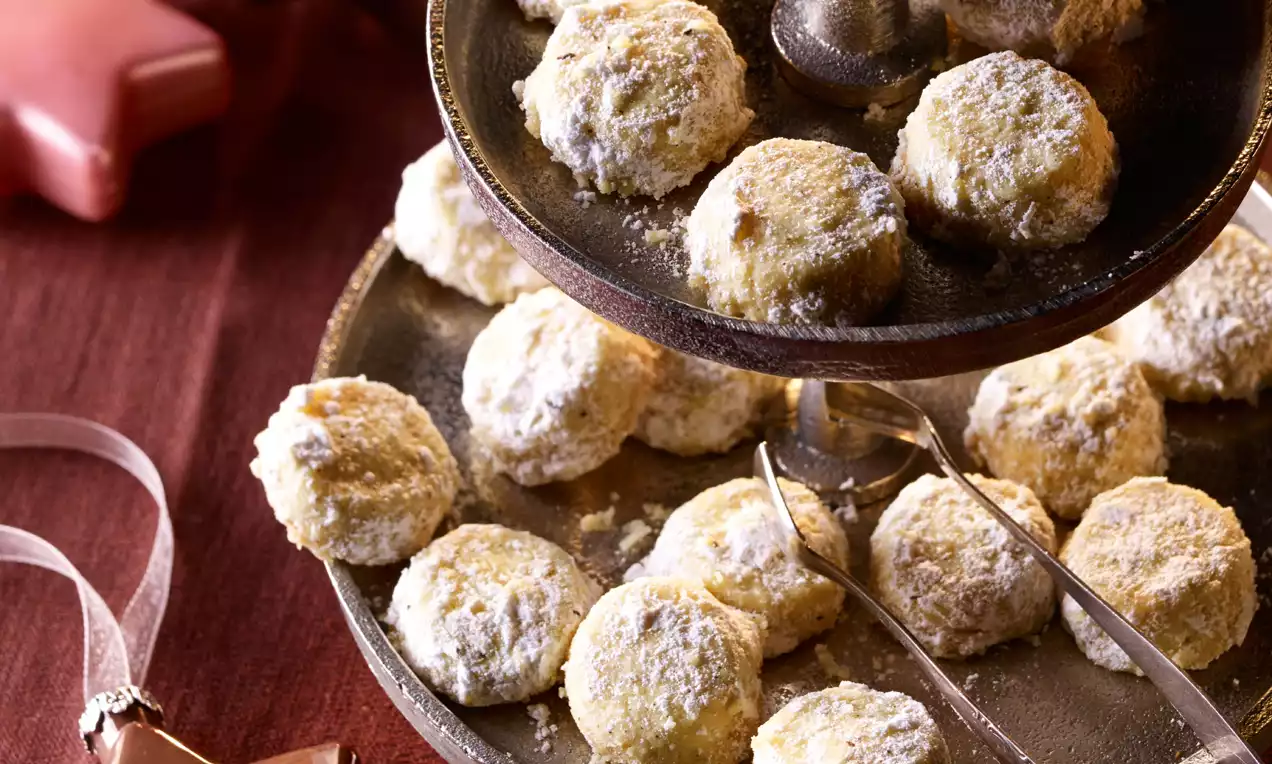 Hellgoldene, runde Vanille-Mürbchen mit feinem Puderzucker bestäubt, kunstvoll arrangiert auf einer mehrstöckigen Etagere aus Metall