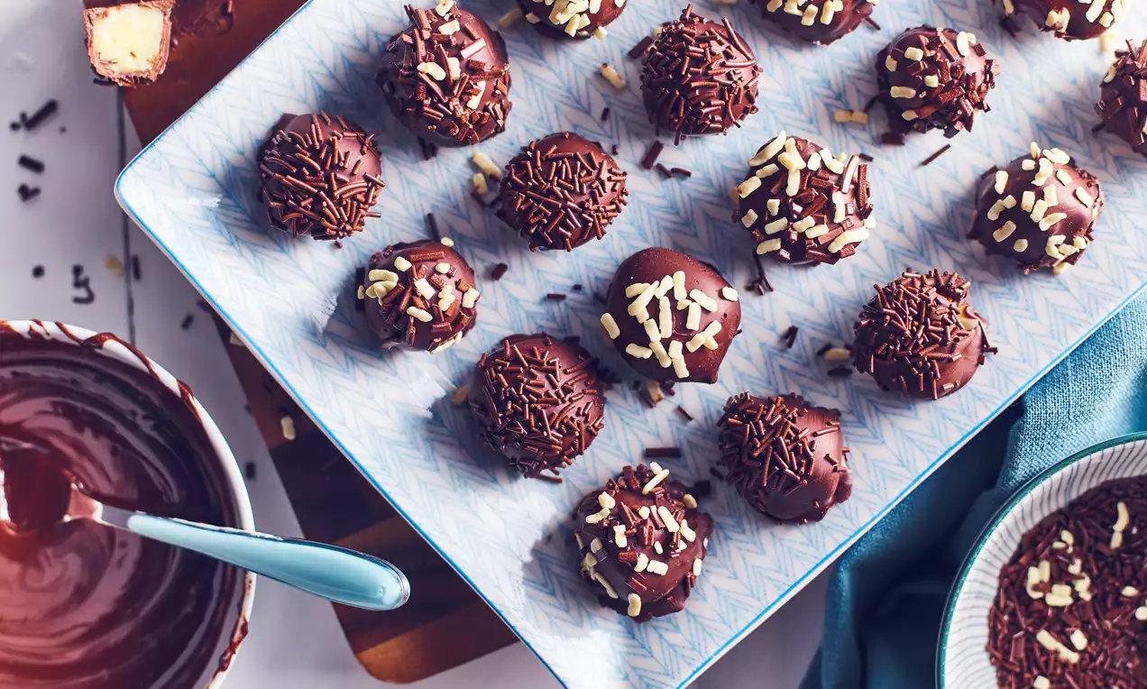 Round chocolate truffles coated with glossy chocolate, sprinkled with chocolate and white flakes, arranged on a patterned platter
