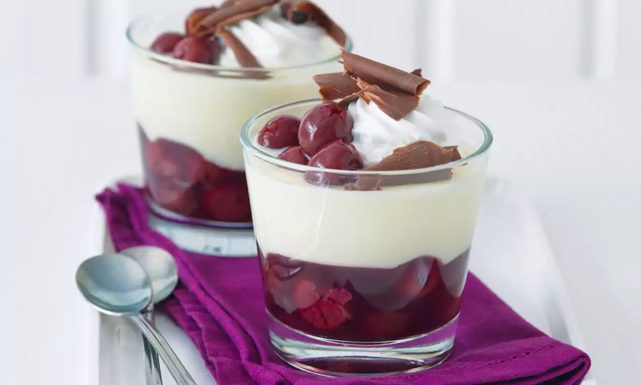 Dvouvrstvé dezerty ve skleničkách, spodní vrstva z tmavě červených višní, světlý krém nahoře, ozdobené šlehačkou, višněmi a čokoládovými hoblinami