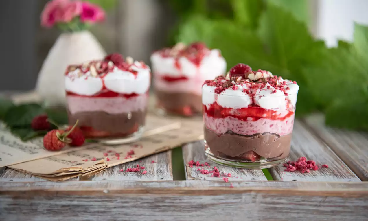 BB pohár s mascarpone v priehľadnom skle, navrstvený kakaovým krémom, ružovým malinovým pyré, šľahačkou, malinami a drvenými orechmi
