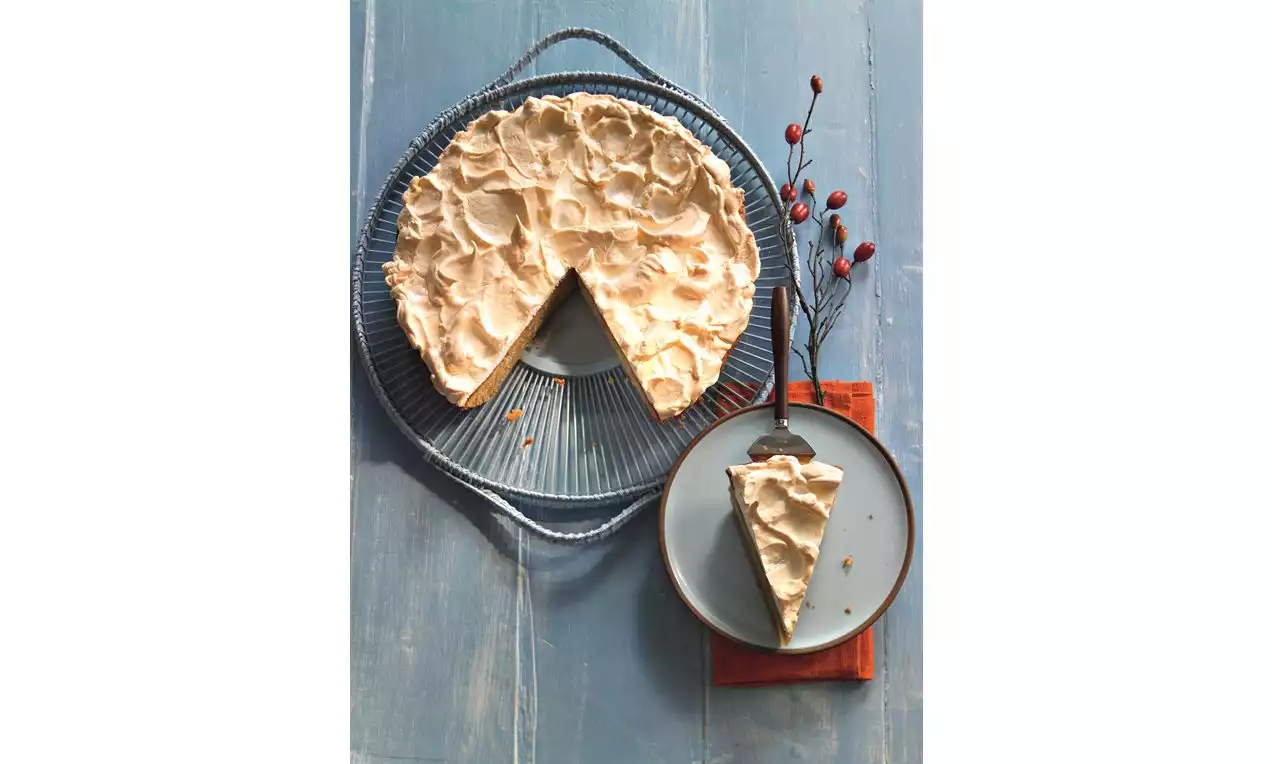 Hruškový koláč zalitý světlým zlatavým sněhem na žebrovaném šedivém talíři, s jedním výřezem na talířku vedle větvičky červených šípků