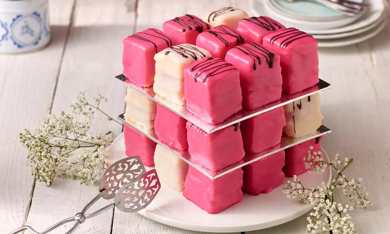 Kleine rosa und weiße Punschkrapfen mit Schokoladenstreifen auf versetzten Silberplatten, dekoriert mit zarten weißen Blüten