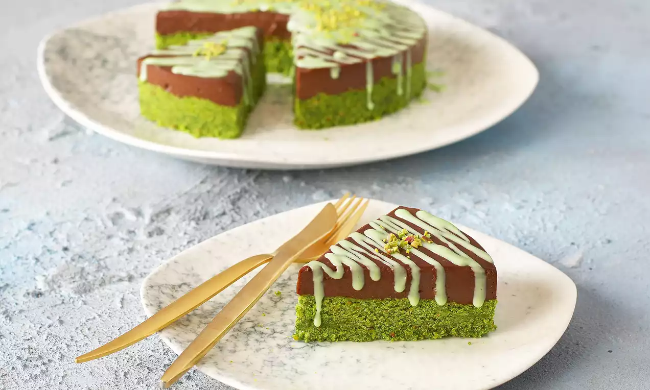 Antep fıstığıyla renklendirilmiş tabanı, koyu çikolata dolgusu ve açık yeşil sos şeritleriyle dekor edilmiş soğuk pasta dilimi