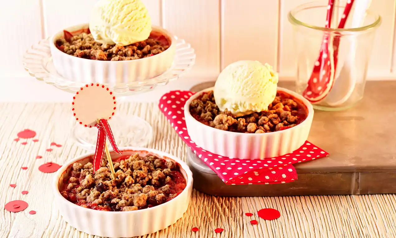 Ahududu dolgusuyla kırmızı beyaz seramik kaplarda sunulmuş crumble tatlıları, üzerlerinde vanilyalı dondurma topları ile düzenlenmiş