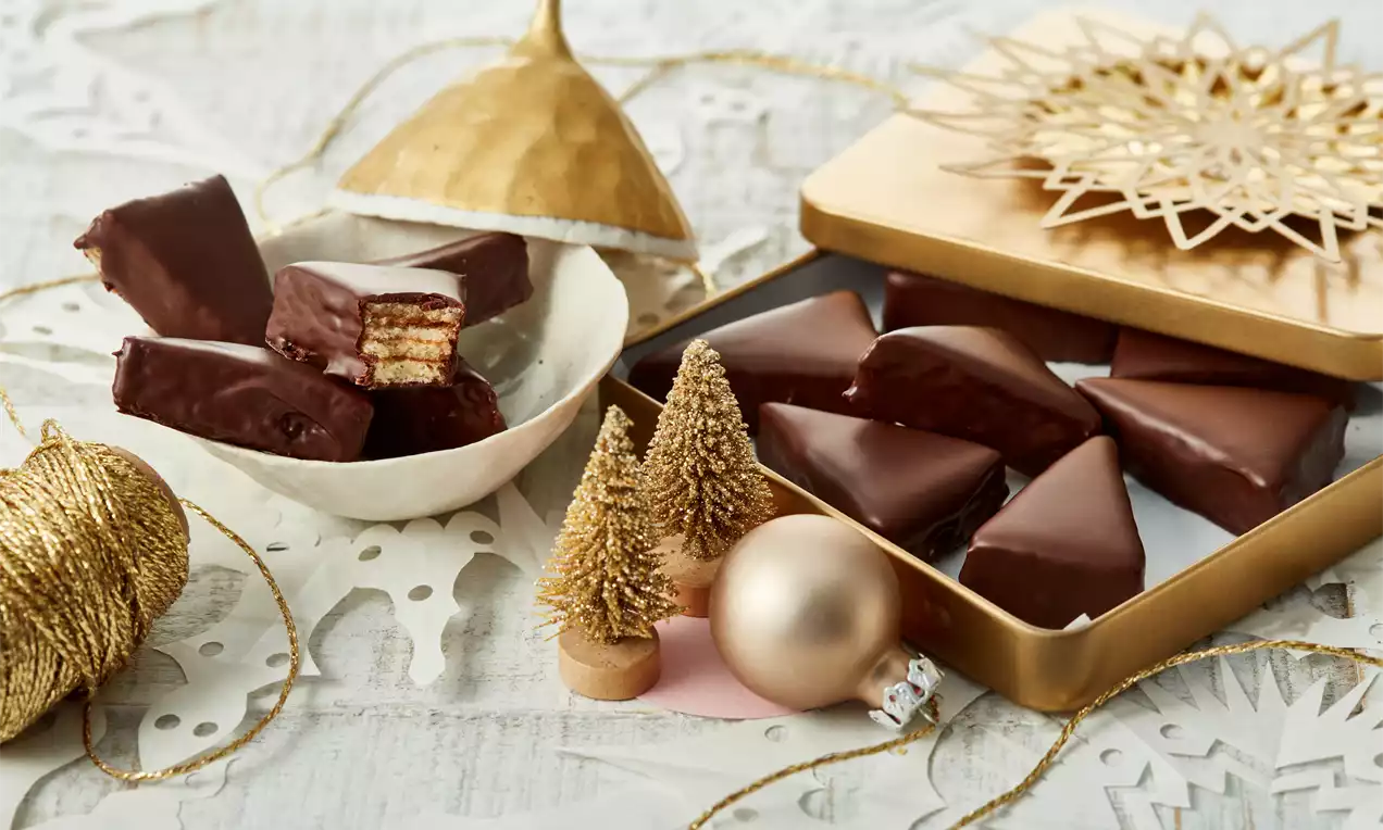 Baumkuchenspitzen mit dunkler Schokoladenhülle, mehrschichtigen Streifen im Inneren, arrangiert in einer goldenen Dose und einer weißen Schale