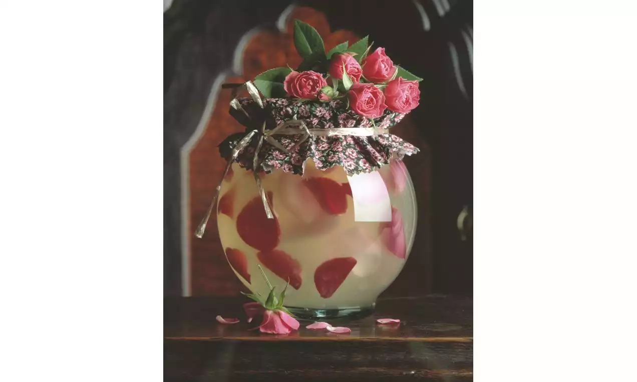 Galaretka z wina musującego w szklanym naczyniu ozdobiona pływającymi płatkami róż, przykryta materiałem w kwiaty, na tle ciemnego drewna  