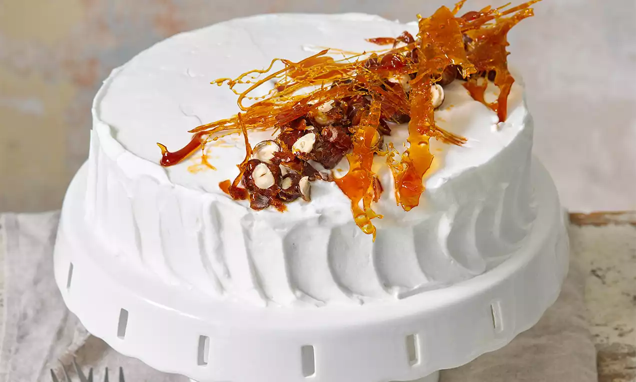 Ořechový dort s karamelovými ozdobami na vrcholu, ve tvaru kulatého korpusu s hladkou bílou polevou na jemně zdobeném talíři