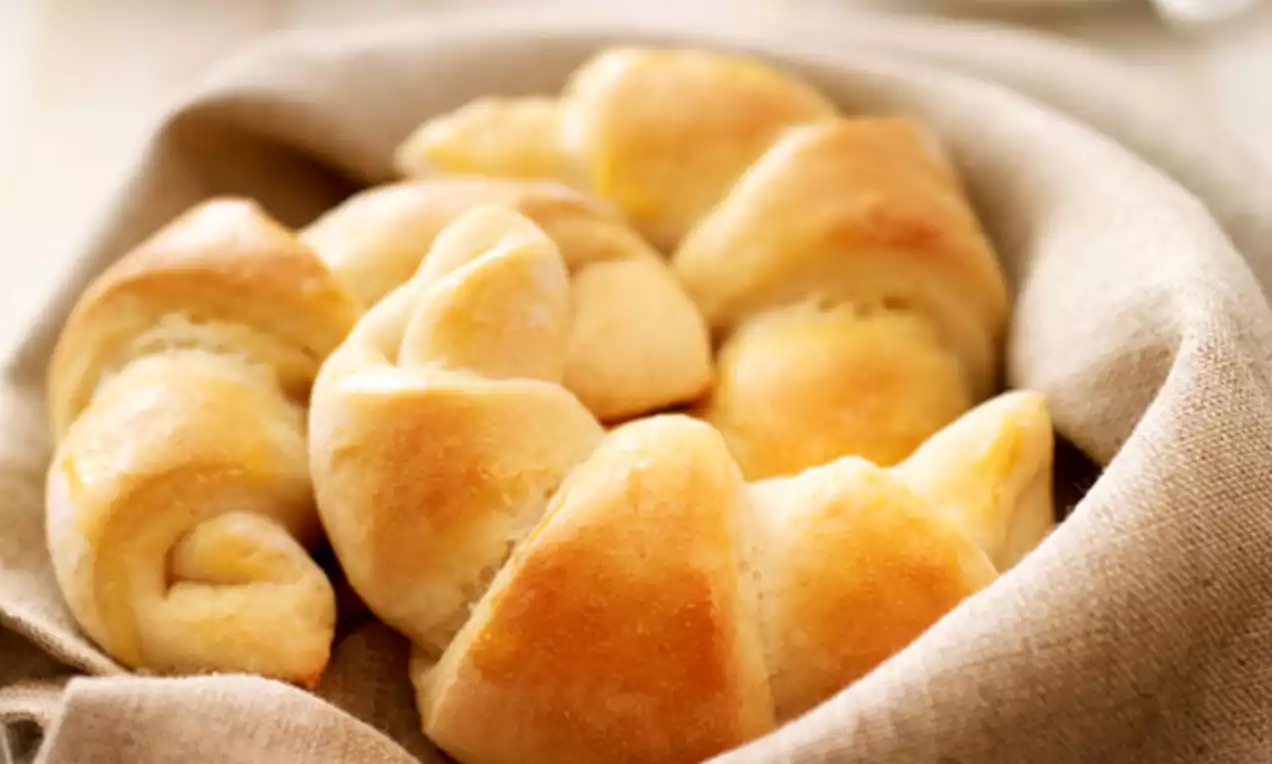 Goudbruine croissants met zachte glans en luchtige textuur, gerangschikt in een beige linnen mand op een lichte houten tafel