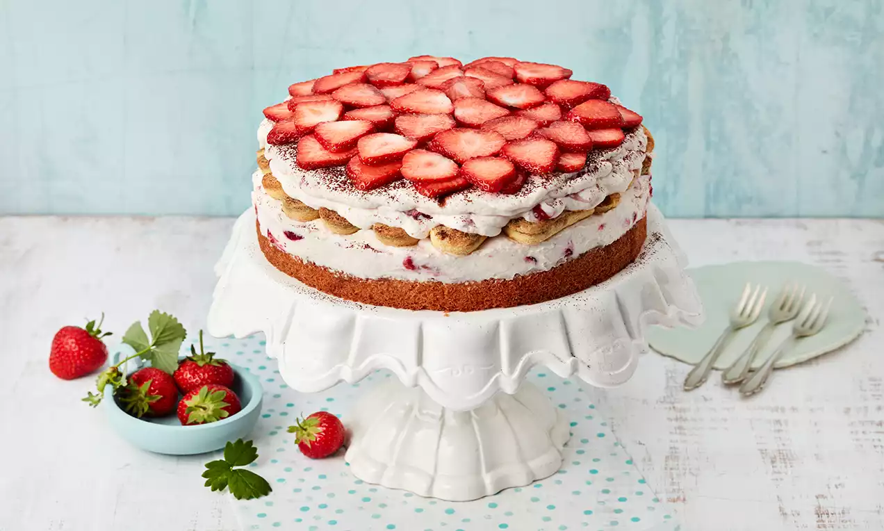 Erdbeer-Tiramisu-Torte mit goldbraunem Boden, luftiger Creme und roten Erdbeerscheiben, serviert auf einer weißen Tortenplatte