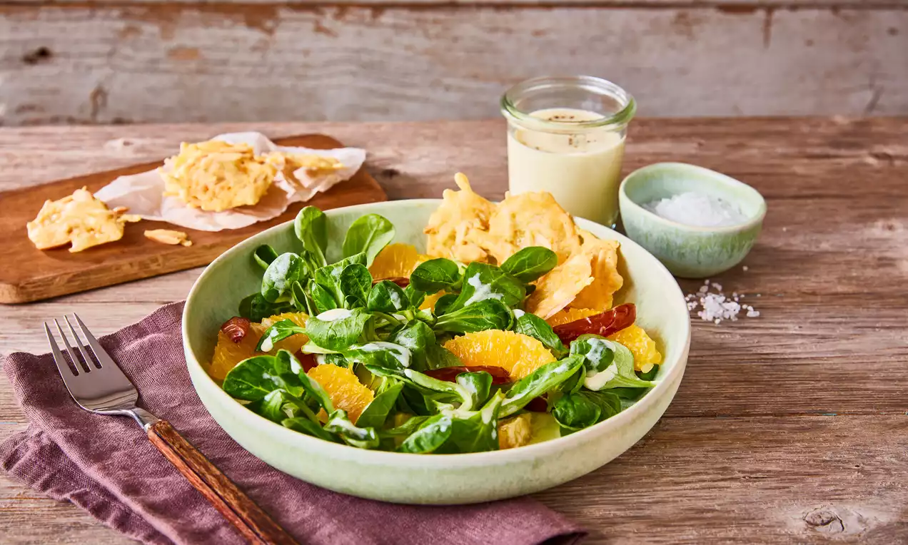 Wintersalat mit Feldsalat, Datteln, Orangenfilets und knusprigen Käsechips, grüne Blätter und orange Segmente angerichtet