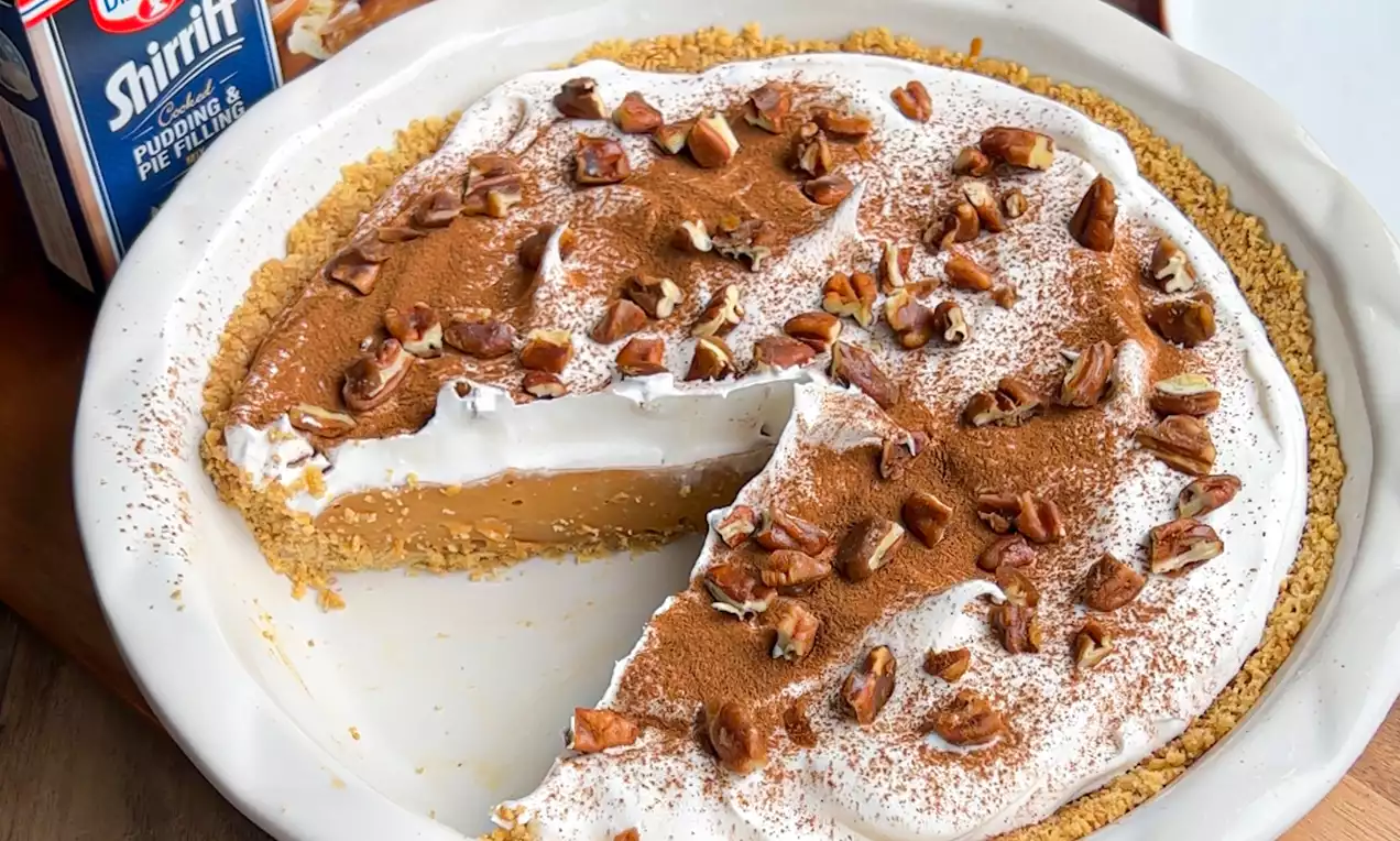 Tarte ronde dans un moule blanc, garnie de crème fouettée, saupoudrée de cannelle et de noix croquantes sur une croûte dorée