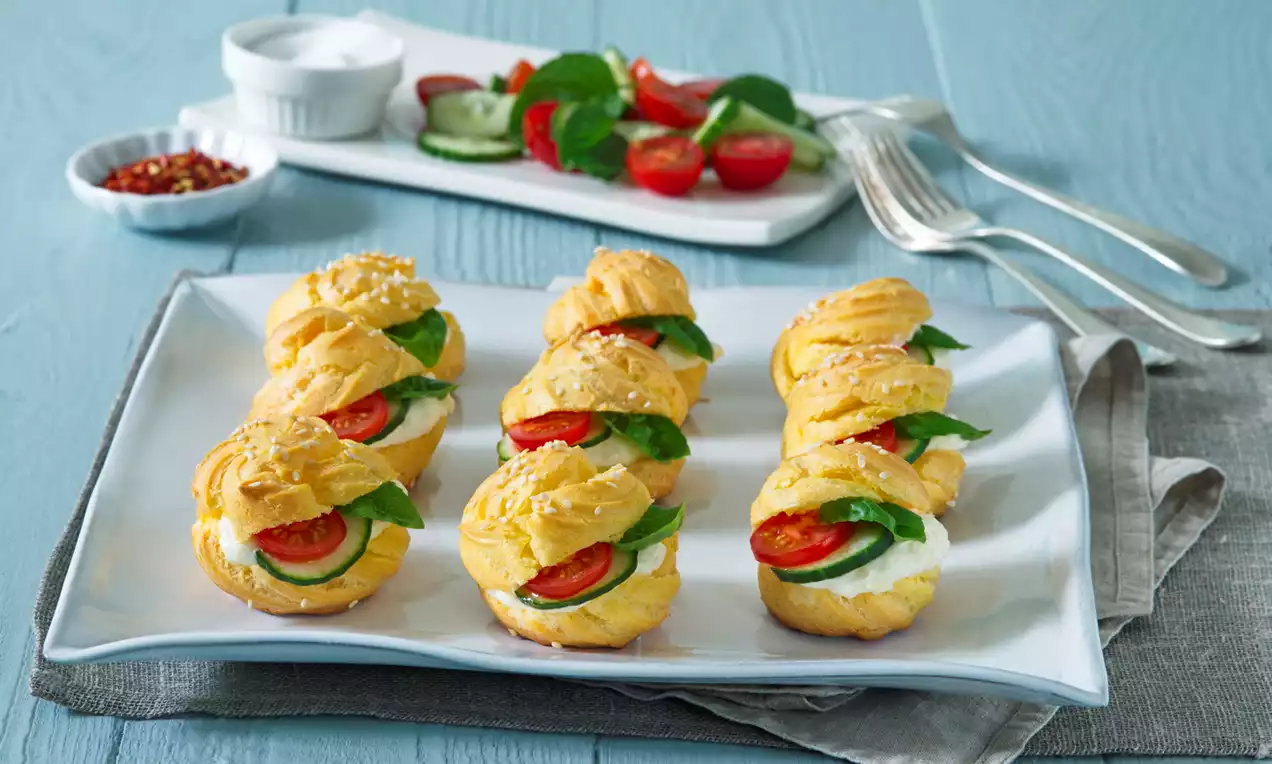 Zlatisté veterníky z jemného cesta plnené krémovým syrom, plátkami paradajok, uhorky a lístkami špenátu na bielom tanieri