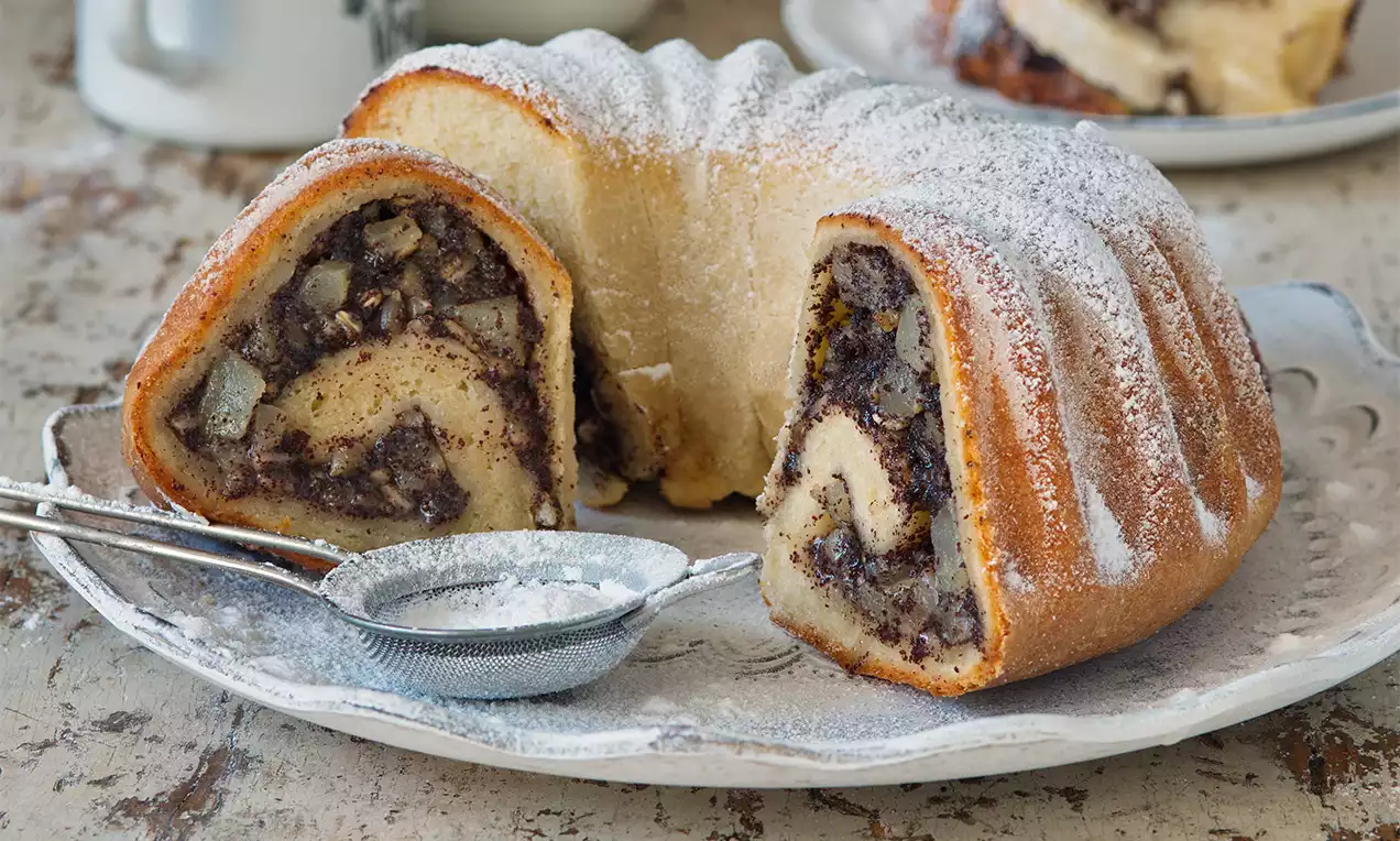 Hruškovo-makový bábovkový závin s jemnou zlatistou kôrkou, plnený šťavnatými hruškami a makom, posypaný práškovým cukrom na porcelánovom tanieri