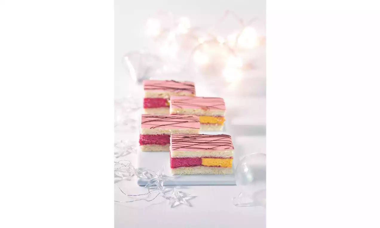 Dvojbarevné vrstvy růžové a žluté piškotové náplně se světlou polevou s čokoládovými proužky, úhledně vyskládané na bílém podkladu