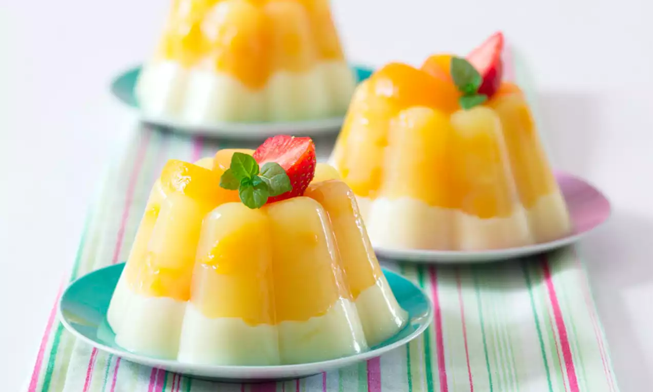 Dvoubarevná želé ve tvaru vroubkovaného kopce, spodní mléčně bílá vrstva, vrchní jasně žlutá s jahodou a lístky máty na barevném podkladu